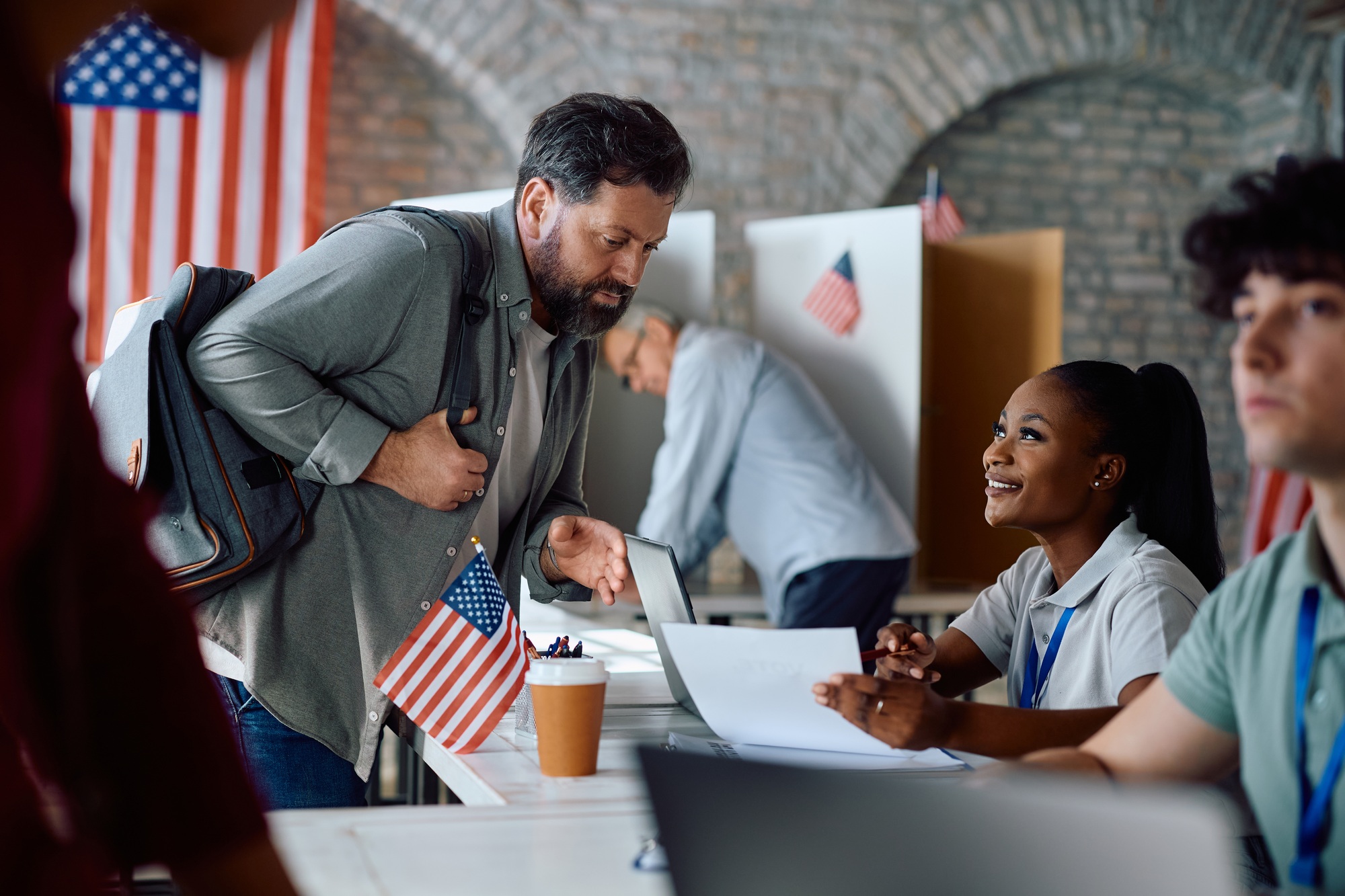 Happy black volunteer talking to a voter during US elections at polling place.